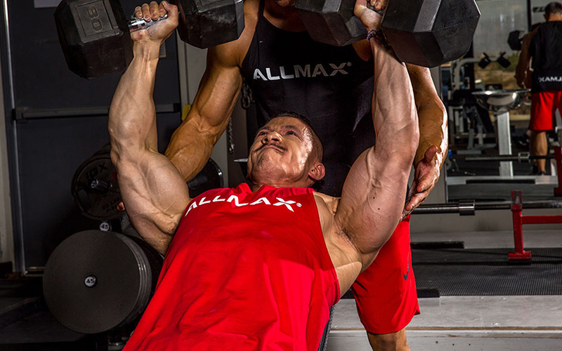 Allmax athlete in red tank performing incline DB press