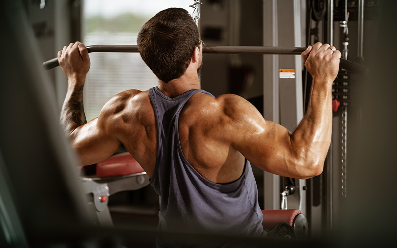 Muscular man wearing a tank top and doing lat pulldowns in the gym