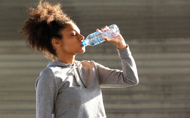 Lean African American female working out outside and drinking water