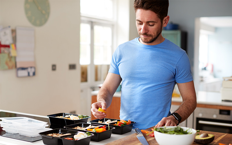 Man in his thirties cooking healthy meals at home in kitchen with containers containers