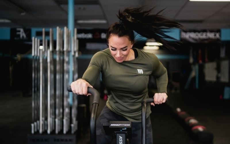 Front shot of a brunette female athlete doing cardio on the assault bike in the gym