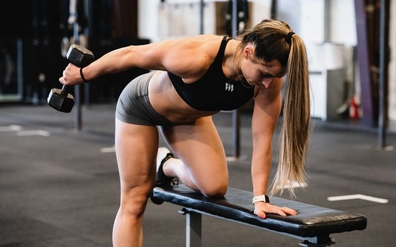 Strong female athlete doing dumbbell tricep kickbacks in the gym
